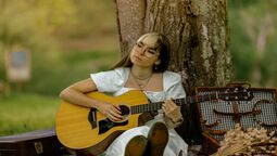 Mioh est assise contre un tronc d'arbre, guitare acoustique à la main, la tête penchée sur le côté. Elle porte une robe blanche, les cheveux longs, chatains et détachés avec une frange blonde