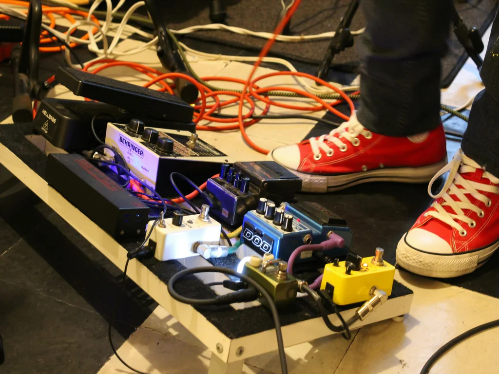 Un pédalier d'effets pour guitare électrique sur lequel est posé un pied qui porte une converse rose