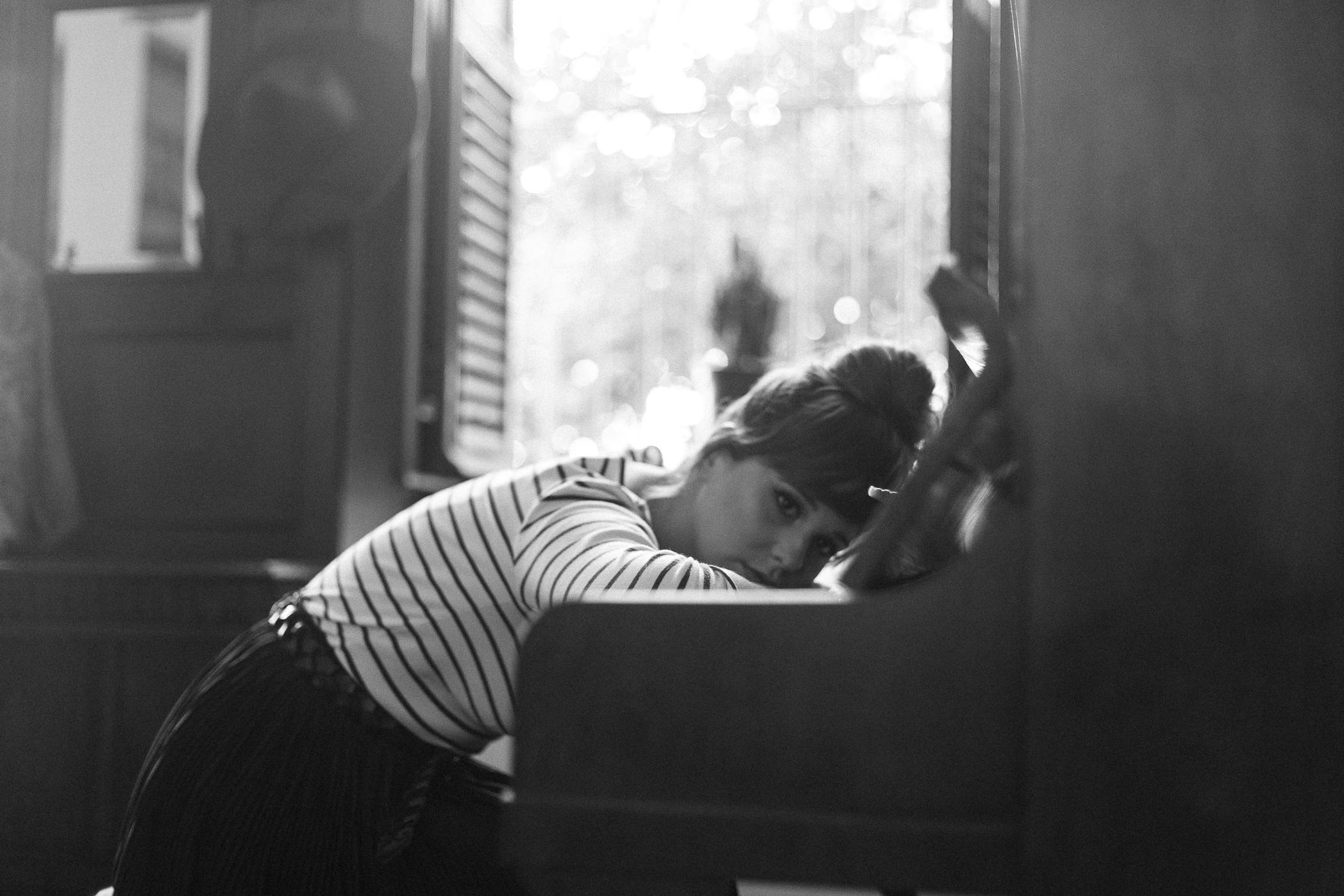 une femme blanche est appuyée sur ses bras, posés contre les touches d'un piano. La photo est en noir et blanc